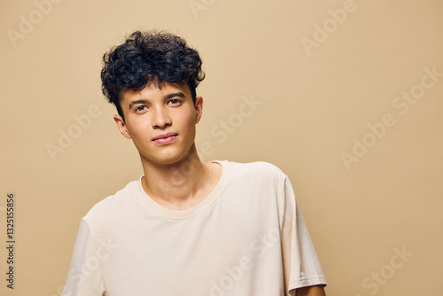 Fotografie Young man with curly hair smiling, wearing a casual beige t shirt against a warm