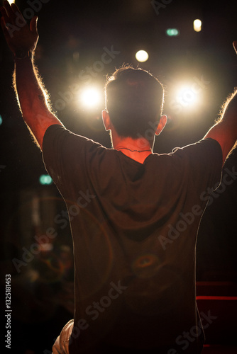 Artiste de dos saluant son public avec les bras ouverts sur une scène et face aux projecteurs