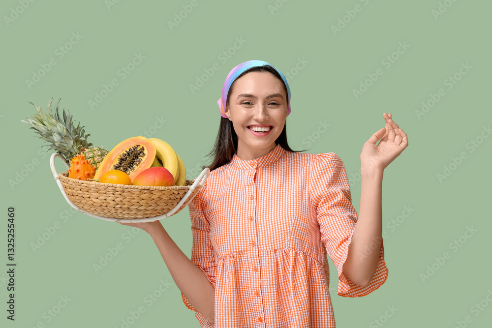 Φωτογραφία Beautiful young woman holding wicker basket with exotic fruits on green backgrou