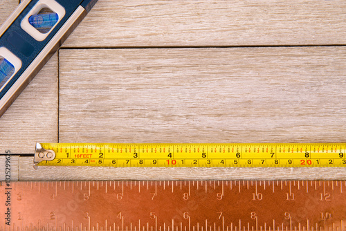 Obraz na płótnie A measuring tape, a ruler, and a level tool arranged on a wooden background. Perfect for themes related to construction, carpentry, home improvement, and professional craftsmanship. w salonie