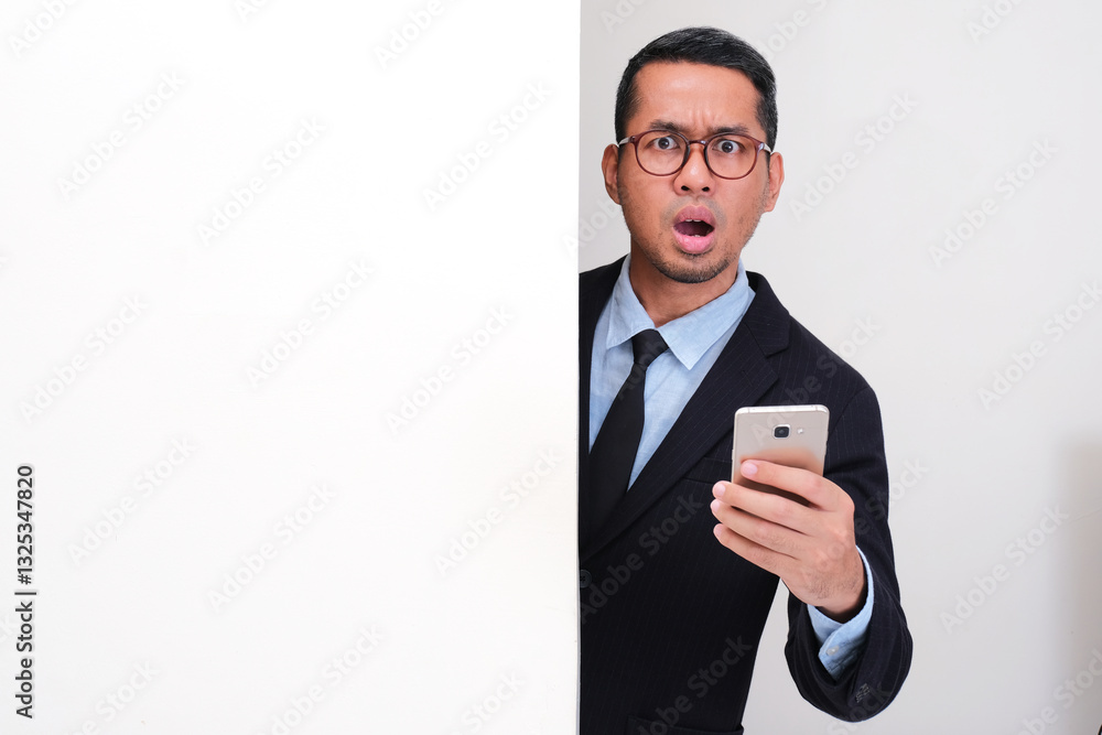 A businessman peeking behind a wall holding mobile phone and showing confused face A businessman peeking behind a wall holding mobile phone and showing confused face