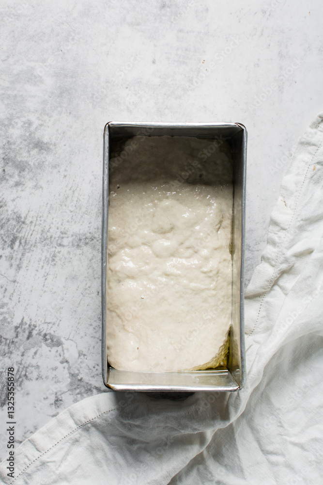 Overhead view of focaccia dough in a loaf baking tin, dough rising in a loaf pan, process of making focaccia Overhead view of focaccia dough in a loaf baking tin, dough rising in a loaf pan, process of making focaccia
