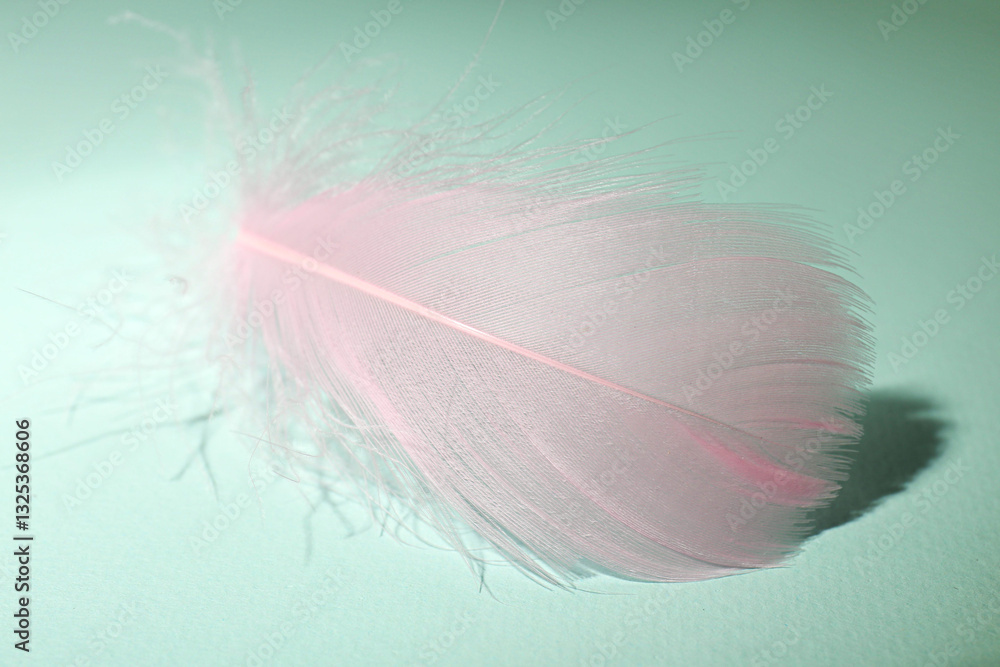Fototapeta premium Fluffy pink feather on light turquoise background, closeup
