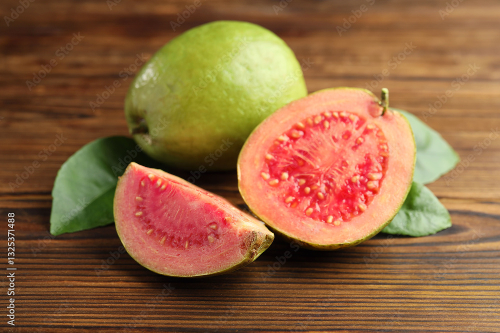 Fototapeta premium Fresh cut and whole guava fruits with leaves on wooden table, closeup