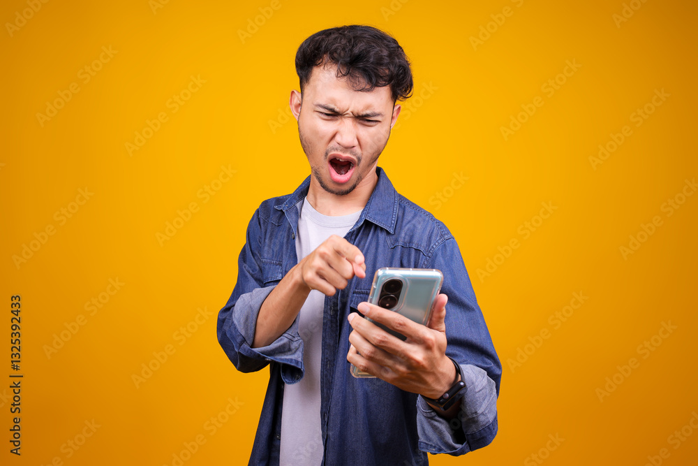 Picture Of Angry Asian Man In Casual Style Screaming And Pointing At Smartphone Over Yellow Background Picture Of Angry Asian Man In Casual Style Screaming And Pointing At Smartphone Over Yellow Background