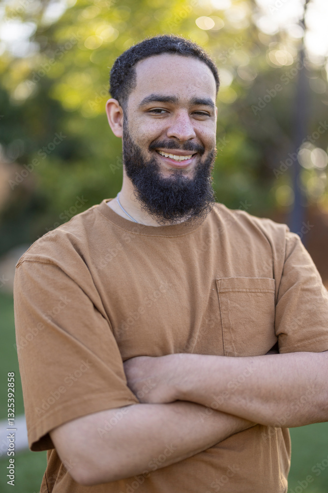 Cheerful African American man poses confidently with arms crossed in a sunny outdoor setting, surrounded by greenery. His friendly demeanor radiates joy, capturing a moment of pure happiness Cheerful African American man poses confidently with arms crossed in a sunny outdoor setting, surrounded by greenery. His friendly demeanor radiates joy, capturing a moment of pure happiness