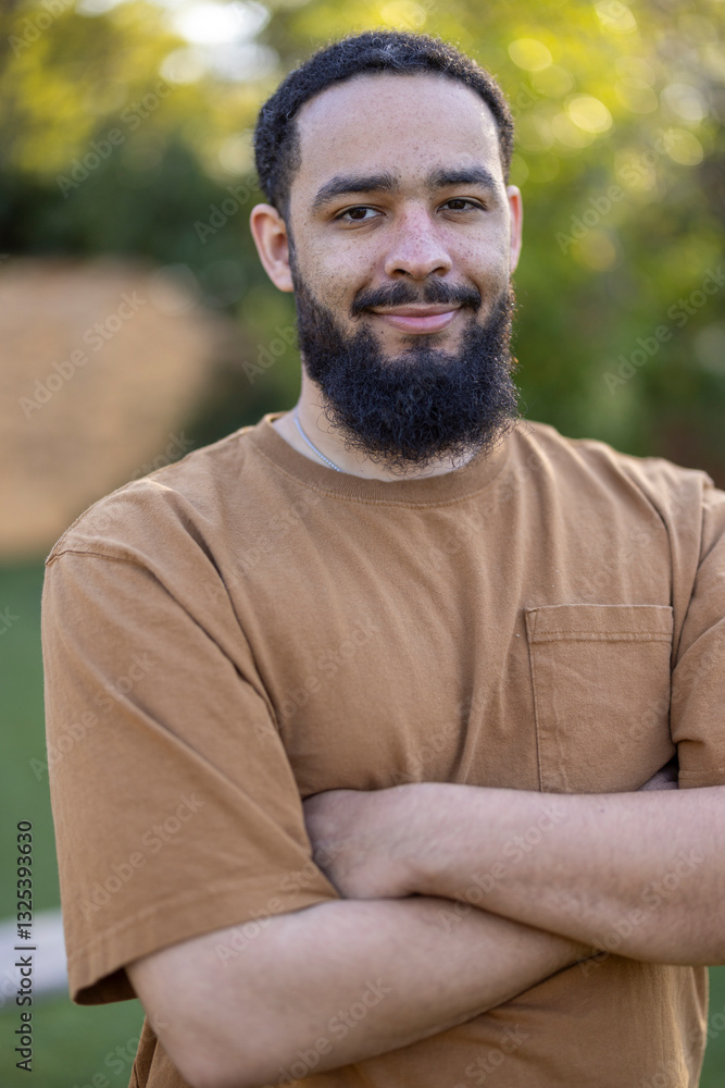A confident man sporting a stylish beard stands comfortably outdoors, with his arms crossed, presenting a casual and laidback demeanor against a backdrop of lush natural greenery and sunshine A confident man sporting a stylish beard stands comfortably outdoors, with his arms crossed, presenting a casual and laidback demeanor against a backdrop of lush natural greenery and sunshine