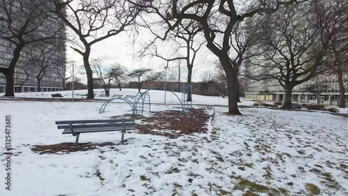 Aerial FPV drone footage of local urban Chicago park during the winter moving swiftly through the snow and playground area into the sprawling cityscape.  