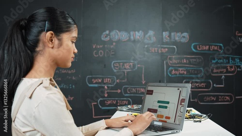 Caucasian girl working on laptop while smiling to camera at blackboard with engineering code and prompt written. Skilled pretty academic student learning programming or coding system. Edification