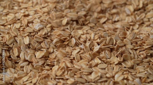 Slow motion, closeup footage of rolled oat flakes pouring over a pile of oats