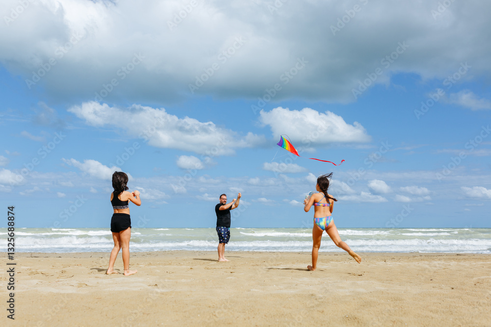 wide angle view of father and two children playing on the beach flying a kite wide angle view of father and two children playing on the beach flying a kite