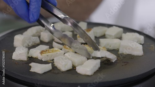 Person flipping halloumi cheese pieces on frying plate close up