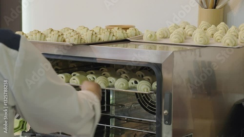 Baker putting plate with raw croissants into electric oven. Bakery concept