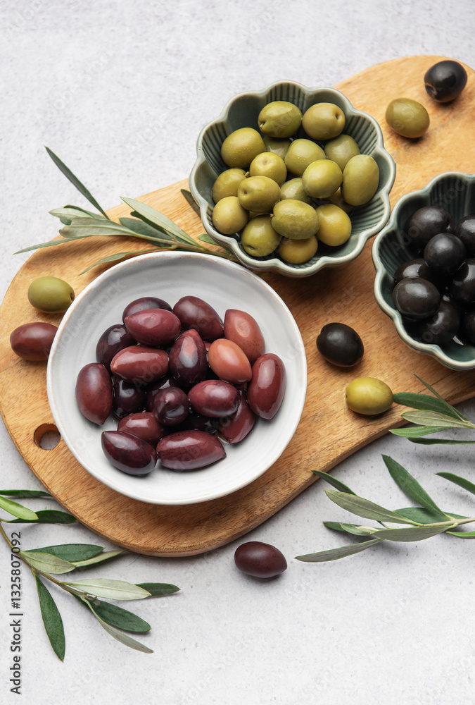 Kalamata, green and black olives displayed on wooden cutting board with olive branches Kalamata, green and black olives displayed on wooden cutting board with olive branches