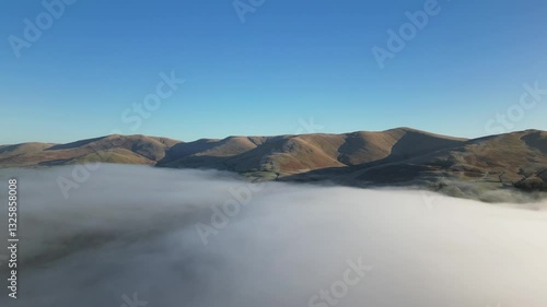 Stunning aerial footage of a drone above the clouds in the UK countryside. The drone emerges from the clouds to see a hill in the lake district at sunrise.