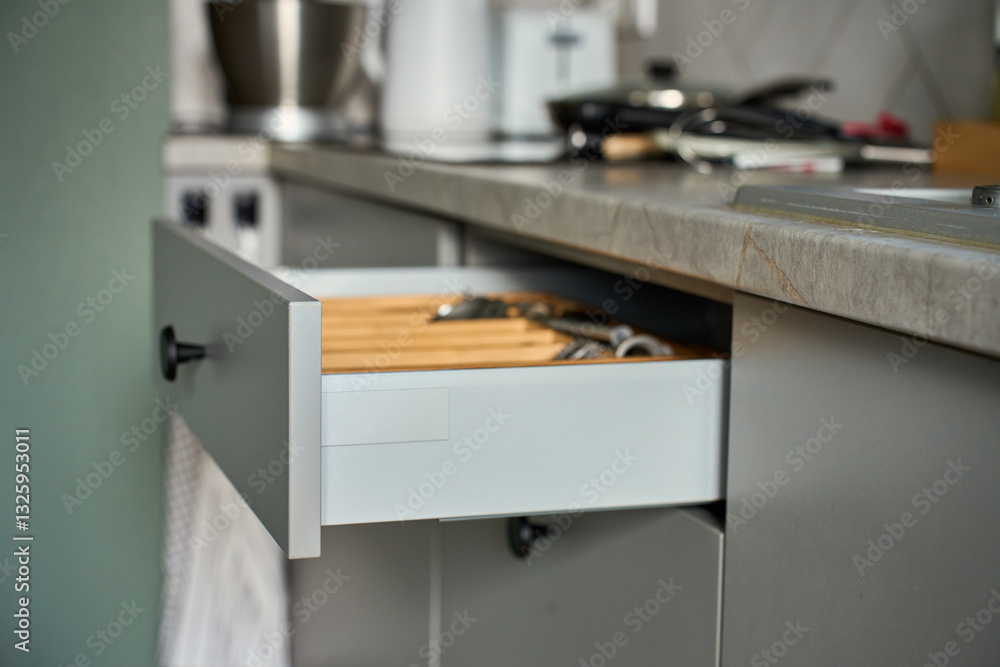 Open kitchen drawer with arranged set of cutlery and cooking utensils in wooden organizer. Contemporary kitchen cabinet. Concept of home organization and kitchen efficiency
