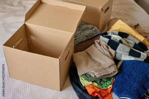 Open donation box with donated clothes on bed. Cardboard box with used clothes for recycling or second hand. Concept of charity, kindness and social responsibility
