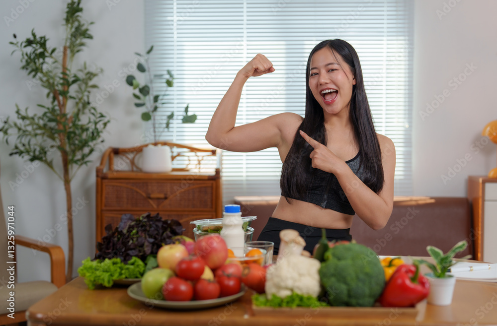 Young asian sportswoman showing muscles and pointing at healthy food on table Young asian sportswoman showing muscles and pointing at healthy food on table