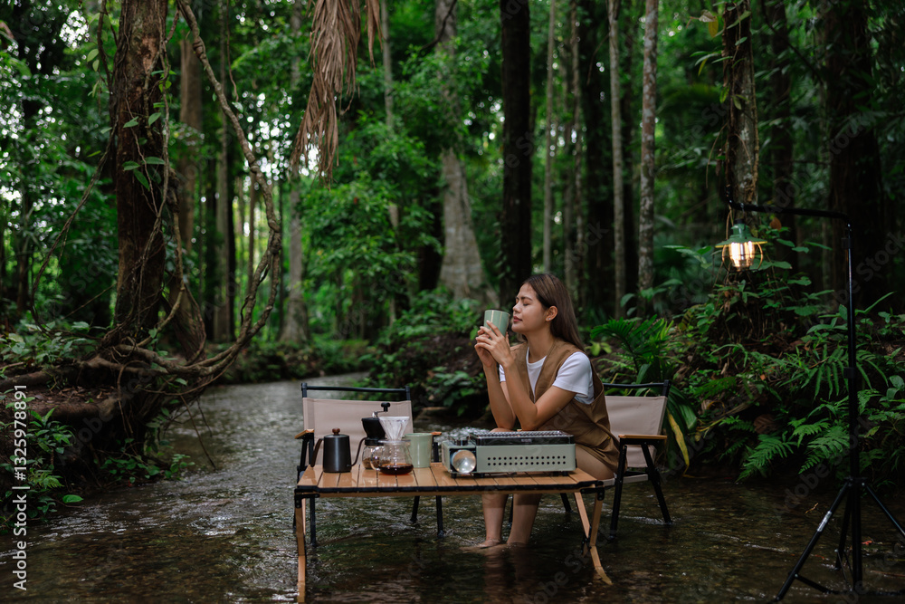 Fototapeta premium asain sitting on chair relax in stream drinking coffee in the morning, camping relax on vacation concept.