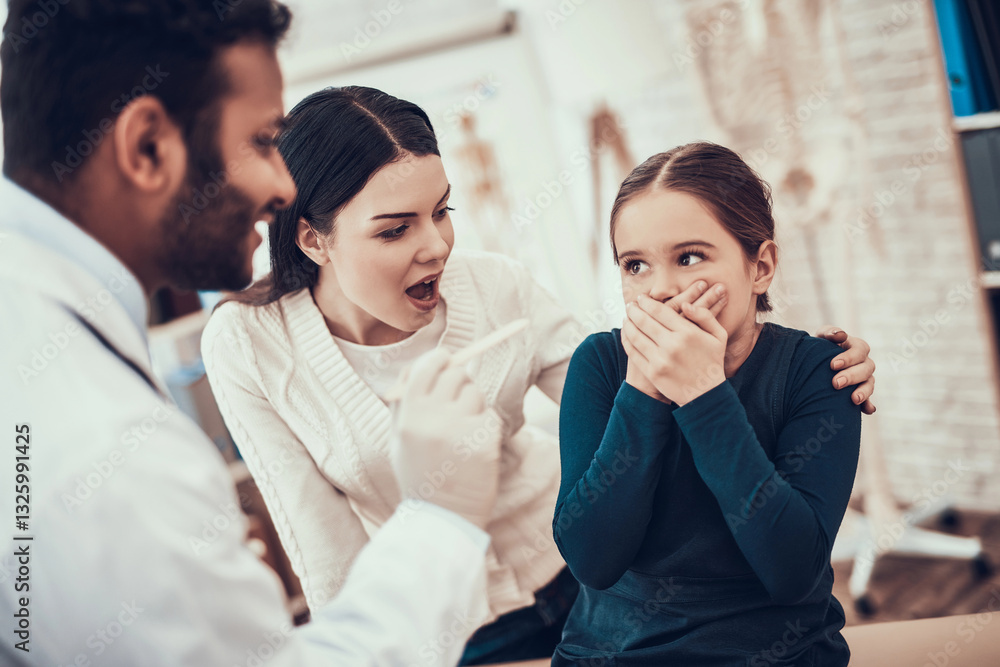 Indian doctor seeing patients in office. Doctor is trying to examine girl's throat but daughter is refusing. Indian doctor seeing patients in office. Doctor is trying to examine girl's throat but daughter is refusing.