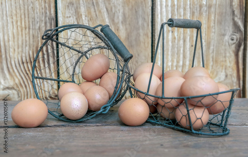 chicken eggs  in little metal baskets on a table in front of a wooden wall .