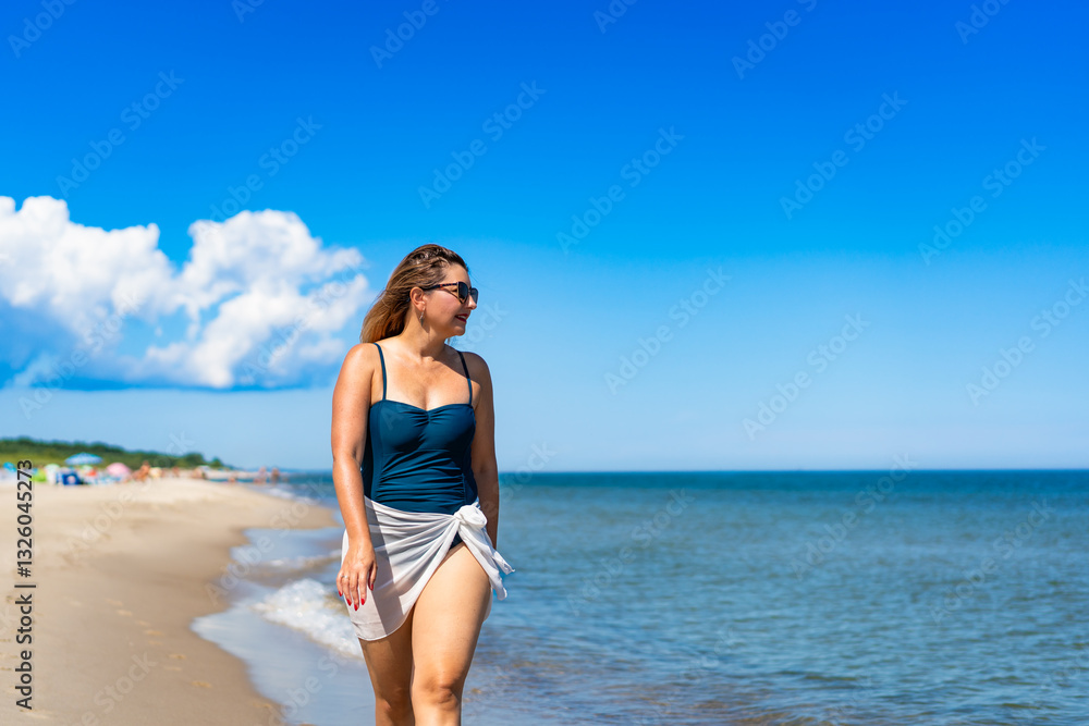 Summer vacation by sea. Beautiful middle aged woman walking along sea on sandy beach on sunny day. Front view Summer vacation by sea. Beautiful middle aged woman walking along sea on sandy beach on sunny day. Front view