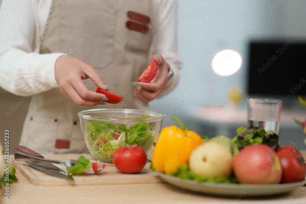 Woman chef adding fresh tomatoes to a healthy salad in glass bowl Woman chef adding fresh tomatoes to a healthy salad in glass bowl
