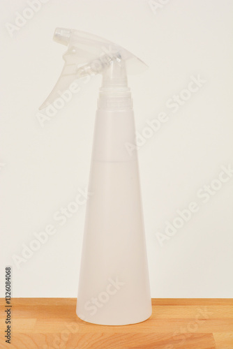 A white plastic spray bottle sits on a wooden surface against a light background