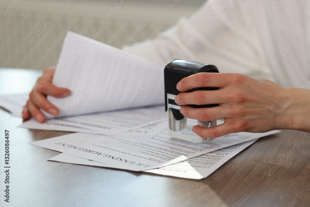 Fototapeta premium Woman stamping licensing agreement document at wooden table indoors, closeup