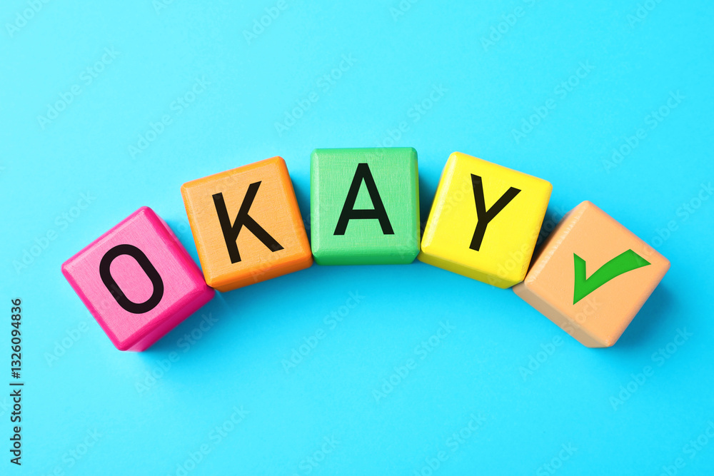 Obraz premium Colorful cubes with word Okay and check mark on light blue background, top view