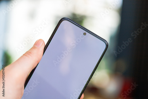 A close-up of a modern smartphone with a blank screen, held in a person's hand. The background is blurred, creating a bokeh effect.