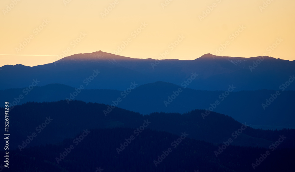 Silhouette of distant mountains at sunset, with golden sky transitioning into deep blue shadows. Ridges and peaks create stunning contrast against warm hues of horizon. Silhouette of distant mountains at sunset, with golden sky transitioning into deep blue shadows. Ridges and peaks create stunning contrast against warm hues of horizon.