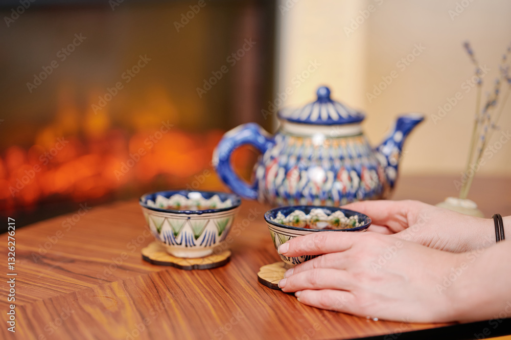 Fototapeta premium Blue ceramic teapot with matching cups placed near warm fireplace, showcasing serenity and refined cultural aesthetics