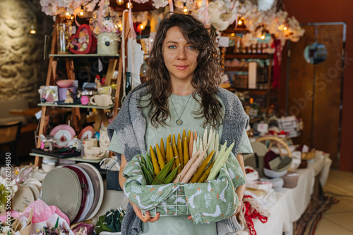 Artisan organizing handcrafted decor at a market stall.  Colorful handmade candles, flowers, and decor at craft fair.