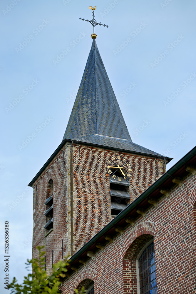 Fototapeta premium A countryside church tower with a spire and cross against a blue sky