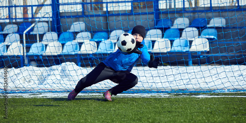 Goalkeeper's Reaction Save. Young goalie diving to intercept ball, displaying concentration, agility, and quick reflexes in soccer defense practice. Concept of protection, reaction, sports mastery.