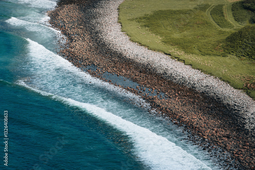 Aerial view of beautiful coastline with waves crashing on rocky shore and grassy terrain, Highlands, Scotland, United Kingdom.