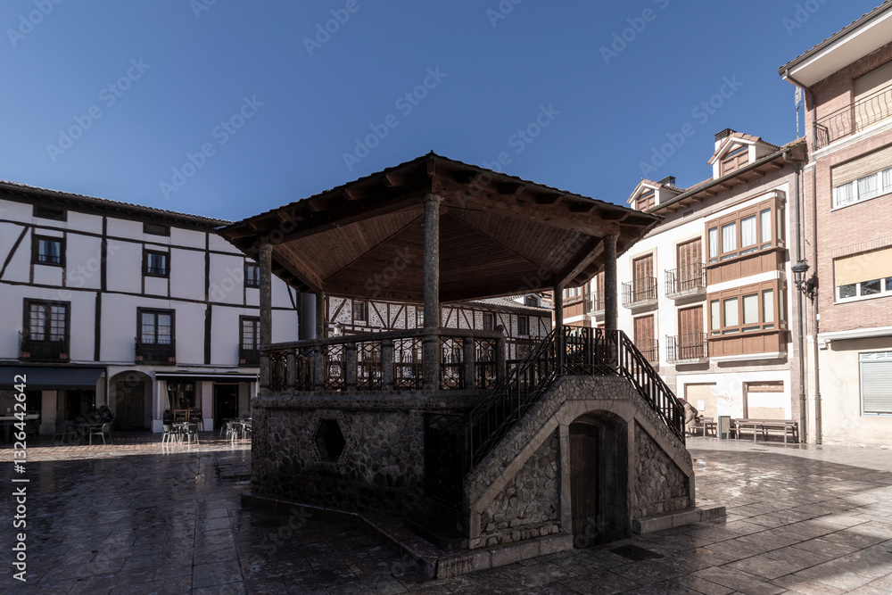 A traditional stone and wood bandstand in a historic European town square, surrounded by half-timbered and modern buildings under a clear blue sky A traditional stone and wood bandstand in a historic European town square, surrounded by half-timbered and modern buildings under a clear blue sky