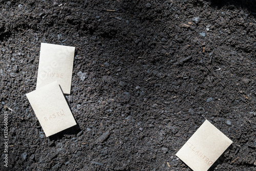 Basil, cilantro, thyme brown seed packets on top of rich, dark, brown fertile soil, planting seeds or gardening background.