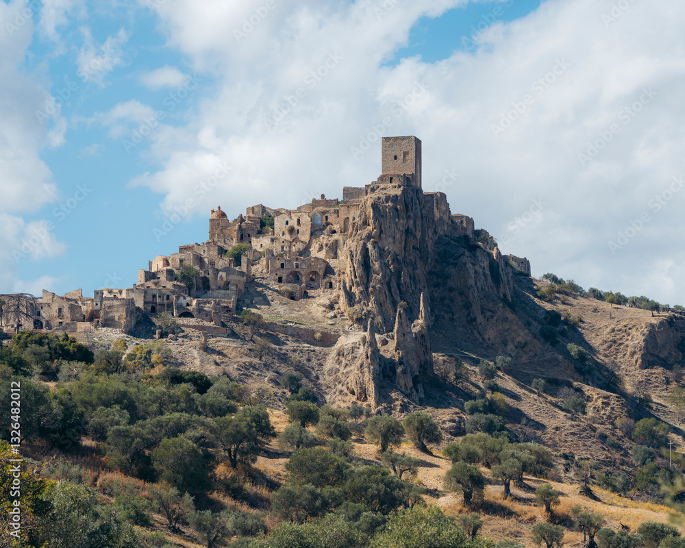 Aerial view of the historic hilltop ruins of Craco surrounded by a scenic landscape with dramatic cliffs and trees, Matera, Italy. Aerial view of the historic hilltop ruins of Craco surrounded by a scenic landscape with dramatic cliffs and trees, Matera, Italy.