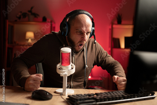 Gamer streamer playing online game on PC in dark room. Yelling angrily and banging fists on the table. Concept of e-Sport Games
