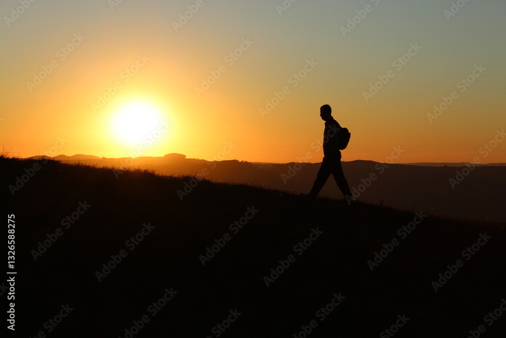 silhueta de homem camimhando em montanha com céu alaranjado ao amanhecer silhueta de homem camimhando em montanha com céu alaranjado ao amanhecer