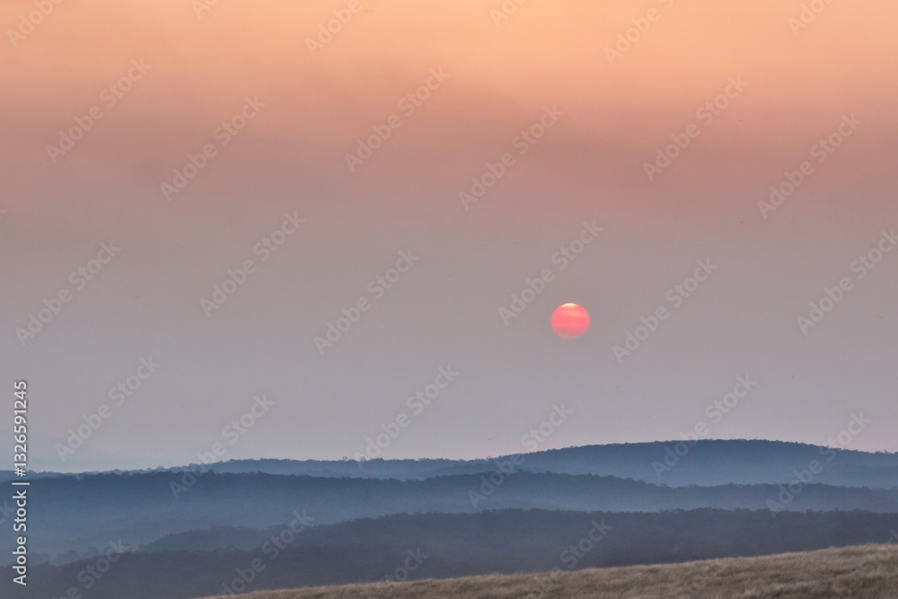 A red Sun sinking into smoke haze over distant mountains A red Sun sinking into smoke haze over distant mountains