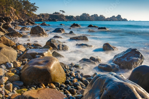 Coast of Korea with round rock formations, a long exposure sea water at sunrise with some vegetation on the shore
