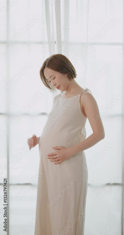 Happy Asian pregnant woman lovingly touching her unborn baby while standing by the window at home. Happy Asian pregnant woman lovingly touching her unborn baby while standing by the window at home.