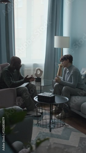 Vertical mirror view of Black male counselor and Caucasian female client discussing emotional challenges in therapy session in modern office