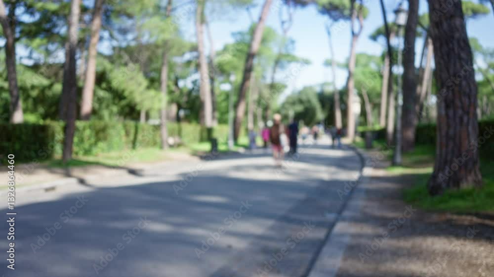 Blurry people strolling through tree-lined paths in villa borghese garden, rome, capturing the serene outdoor atmosphere.