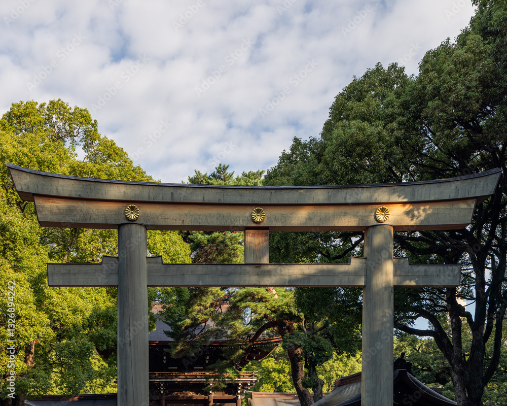 Torii gate of Meiji Shrine in Tokyo crafted from wood and featuring golden chrysanthemum symbols rises against a backdrop of dense foliag Torii gate of Meiji Shrine in Tokyo crafted from wood and featuring golden chrysanthemum symbols rises against a backdrop of dense foliag