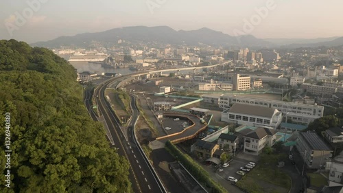 Aerial view of modern urban landscape with expressway, harbor, and mountains at sunset, Sasebo, Nagasaki, Japan.