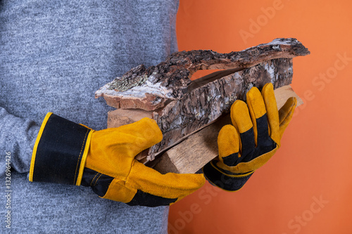 Wallpaper Mural A person wearing yellow work gloves holds pieces of firewood against an orange background, emphasizing safety and outdoor work. Torontodigital.ca